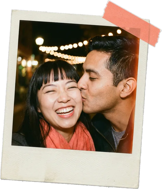 Polaroid photo of a man kissing his laughing partner on the cheek under string lights